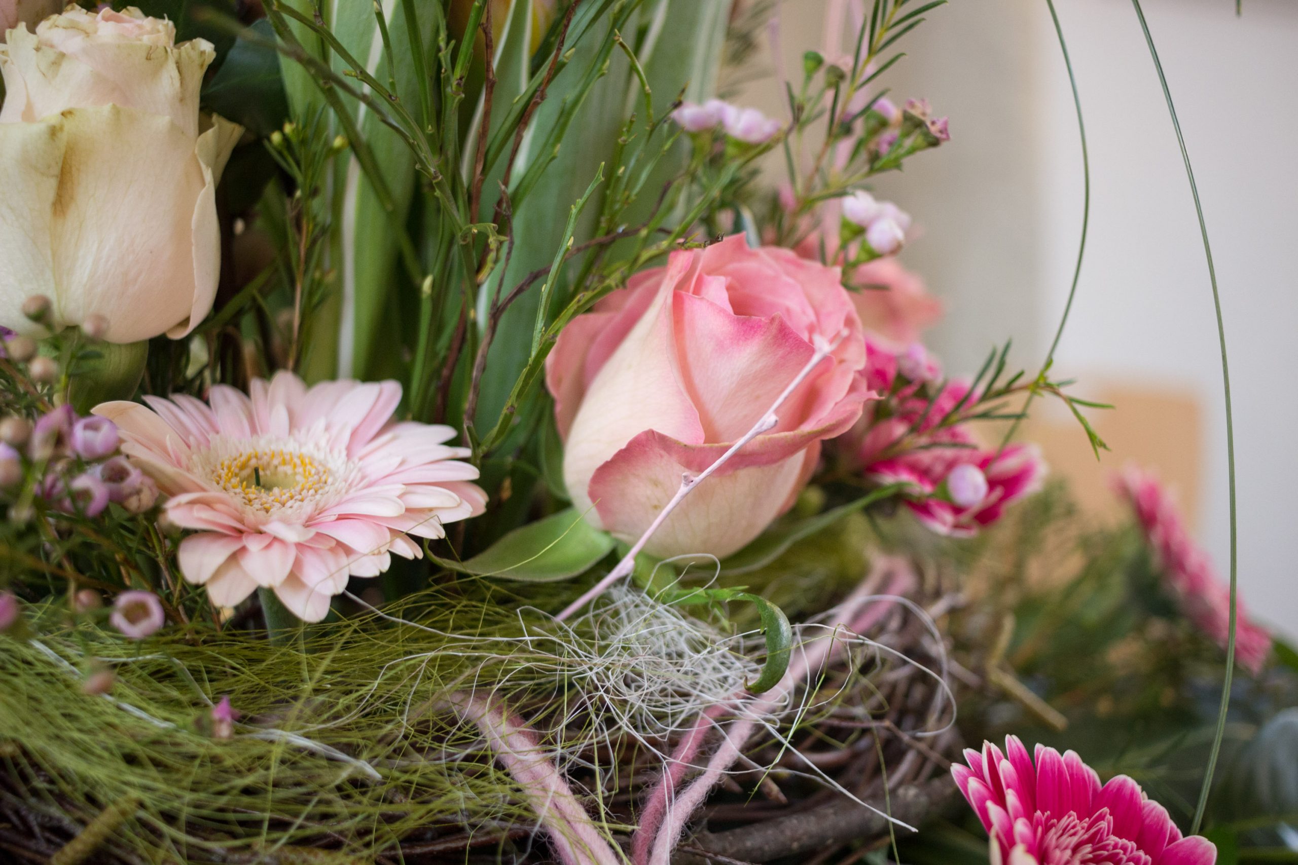 Nahaufnahme eines Blumenstraußes mit rosa und weißen Rosen, Gerbera, Grün und weißen Fäden.